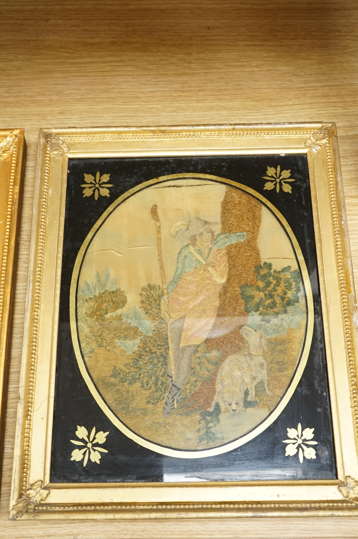 A pair of oval framed early 19th century silk embroideries of a Shepherd and Shepherdess mounted in Verre eglomise glass and gilt frames. Embroideries 28cm high